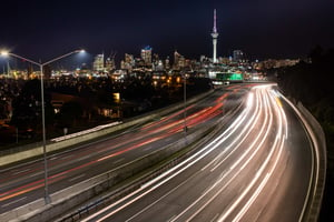 Car light trails at night heading into Auckland, with the city skyline
